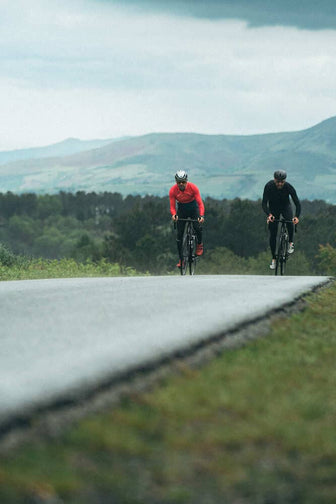 Two men cycling on a road with mountains in the background