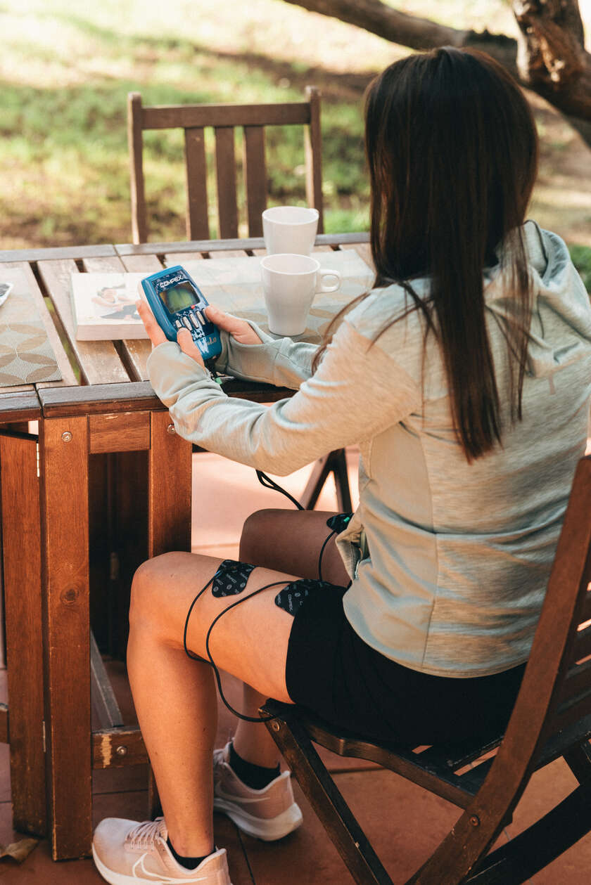 A woman using the Compex FIT 1.0 EMS muscle stimulator to do recovery on her quads